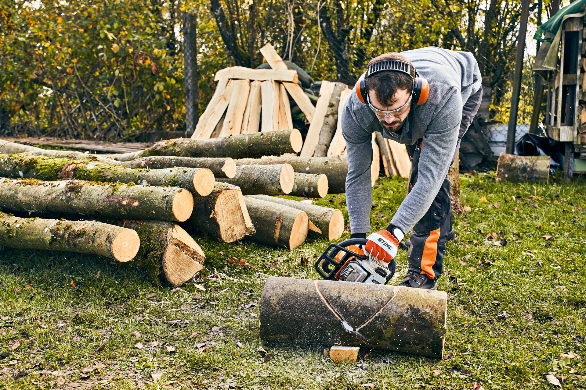 Muž s ochranou sluchu používá motorovou pilu STIHL MS 180 při práci na zahradní lavičce pro kutily.