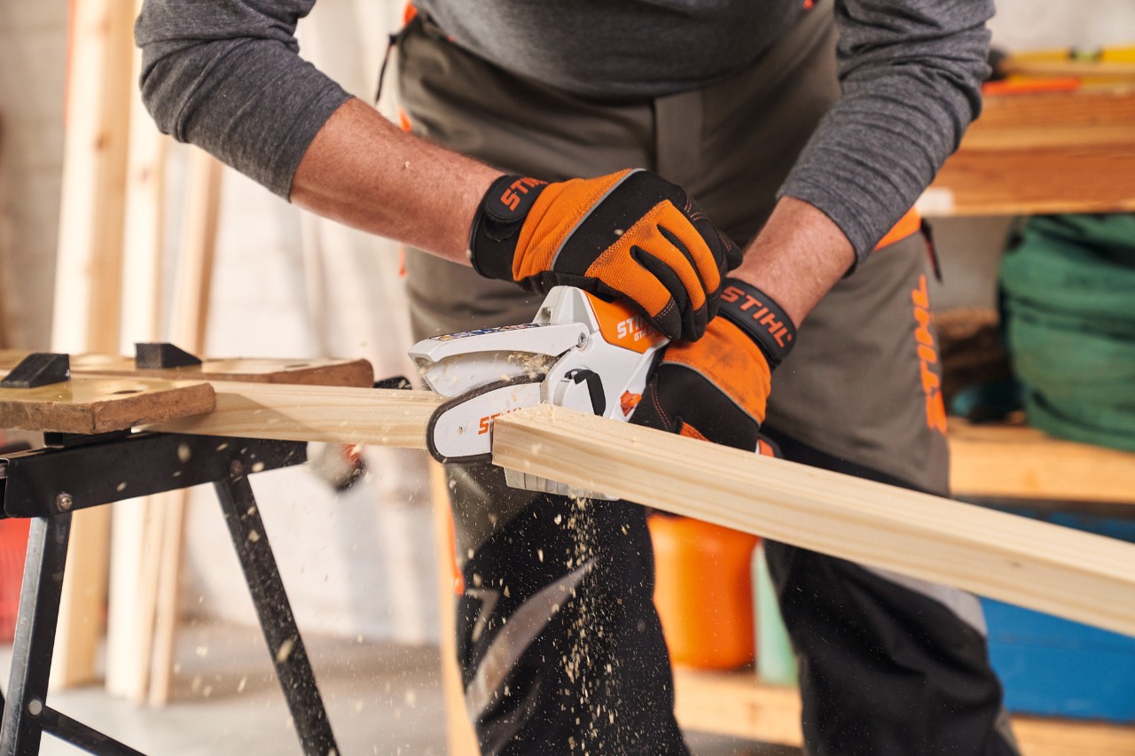 Osoba s ochrannými rukavicemi STIHL Function Protect zkracuje hranoly rámu na zástěnu na ochranu soukromí pomocí vyvětvovací minipily STIHL GTA 26