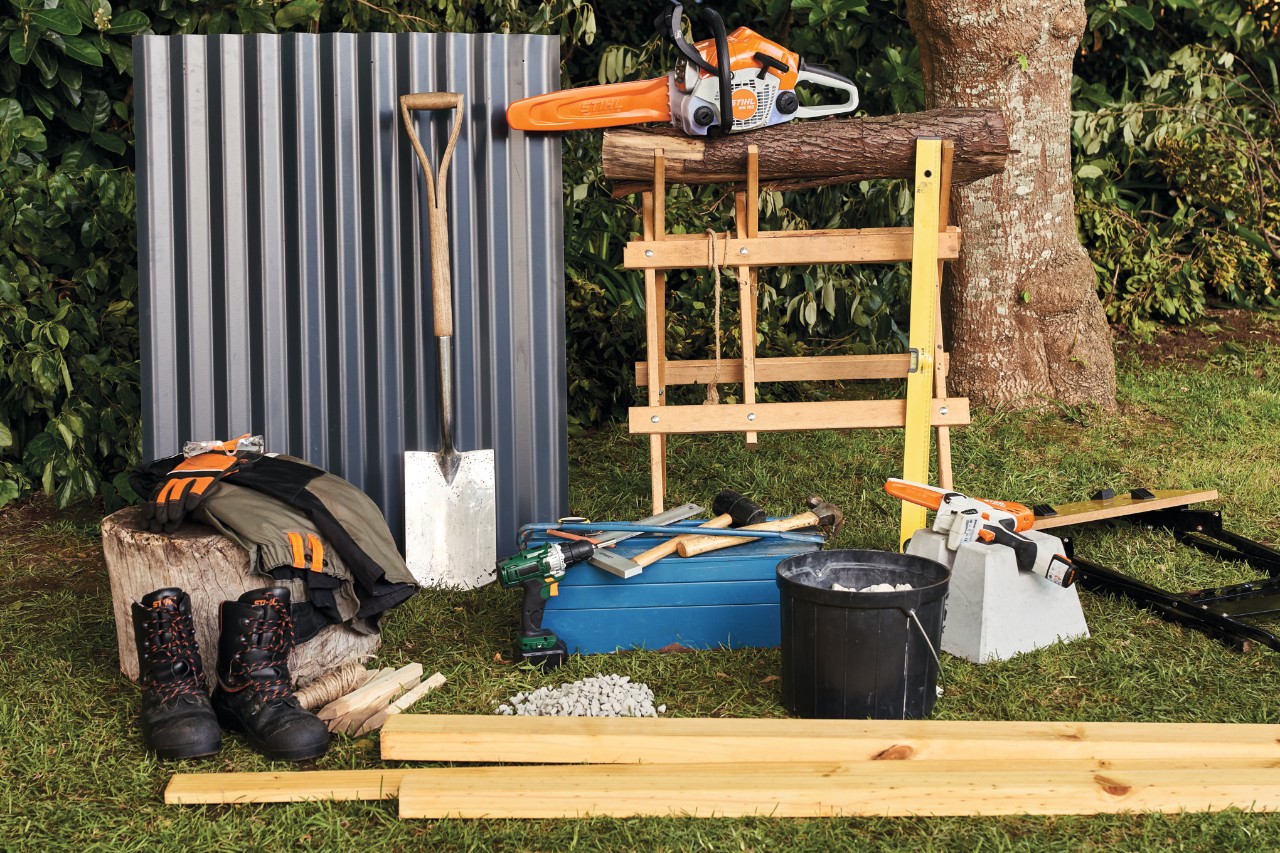 Na zahradě jsou připraveny materiál a nářadí, jako je akumulátorová motorová pila STIHL MSA 140, pro svépomocnou stavbu přístřešku na dřevo