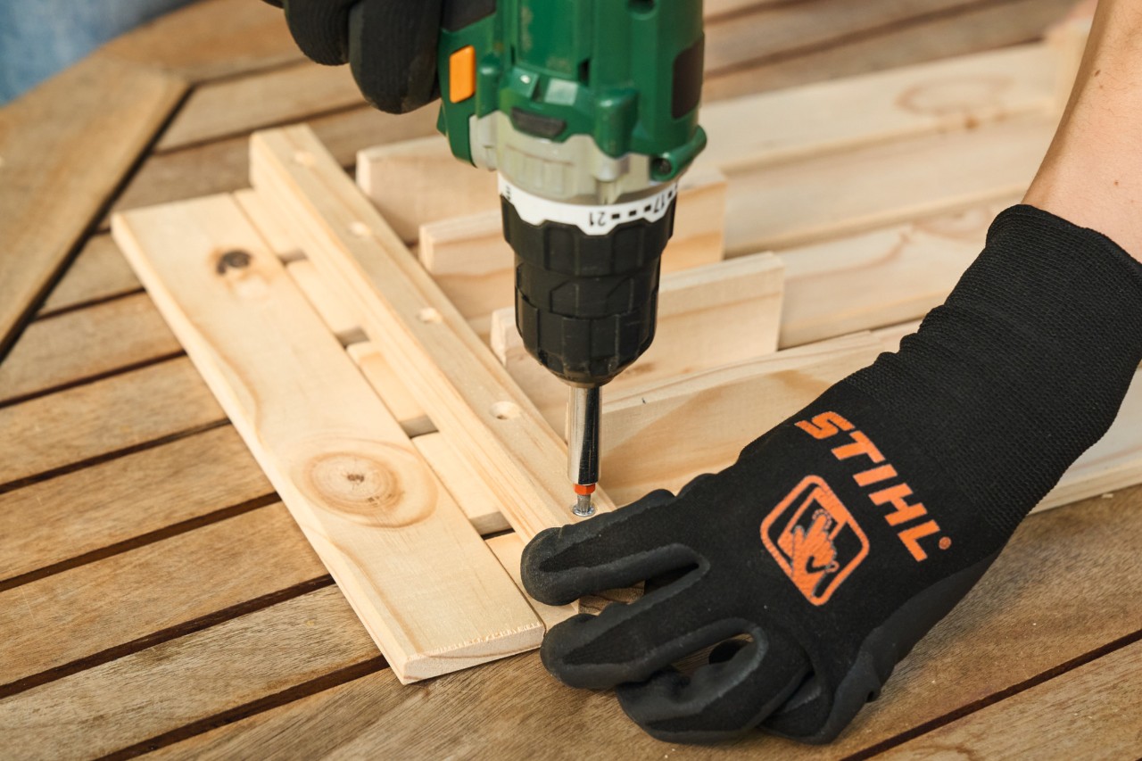 Detailní záběr na osobu v ochranných rukavicích STIHL při předvrtávání otvorů