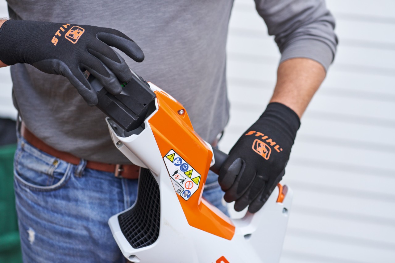 Osoba v černých rukavicích STIHL vyjímá akumulátor z fukaru