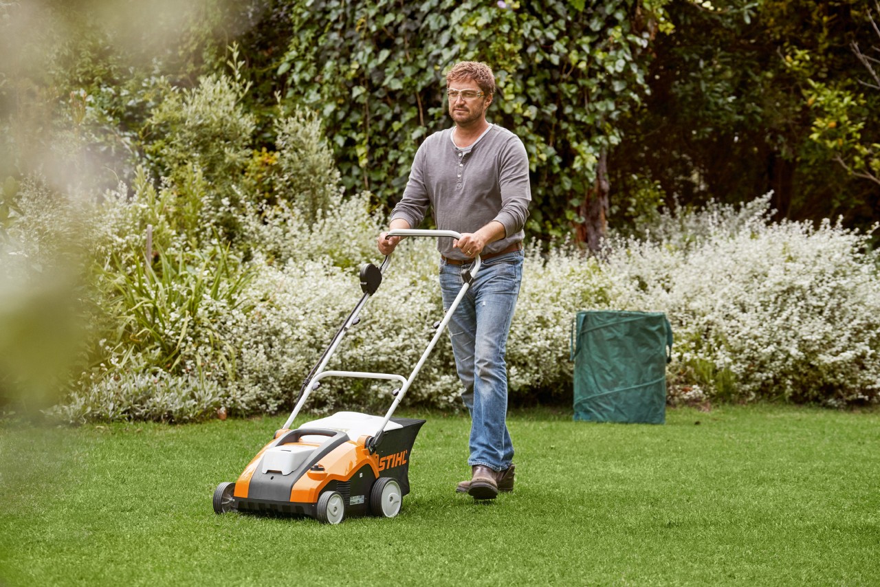 Muž provádí vertikutaci zeleného trávníku pomocí akumulátorového provzdušňovače STIHL RLA 240
