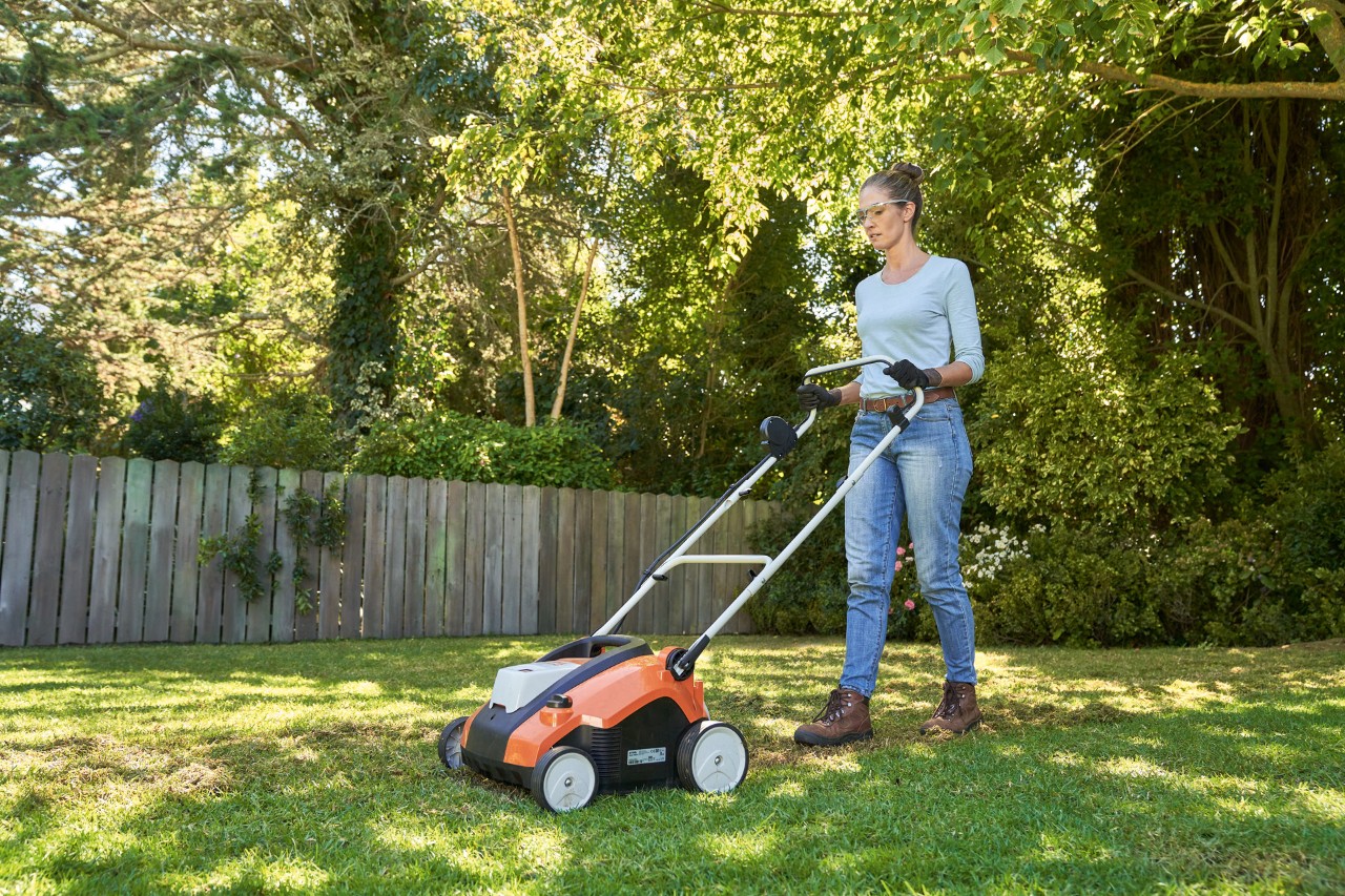 Žena na zahradě provzdušňuje trávník akumulátorovým provzdušňovačem STIHL RLA 240 a je vybavena ochrannými brýlemi a pracovními rukavicemi.