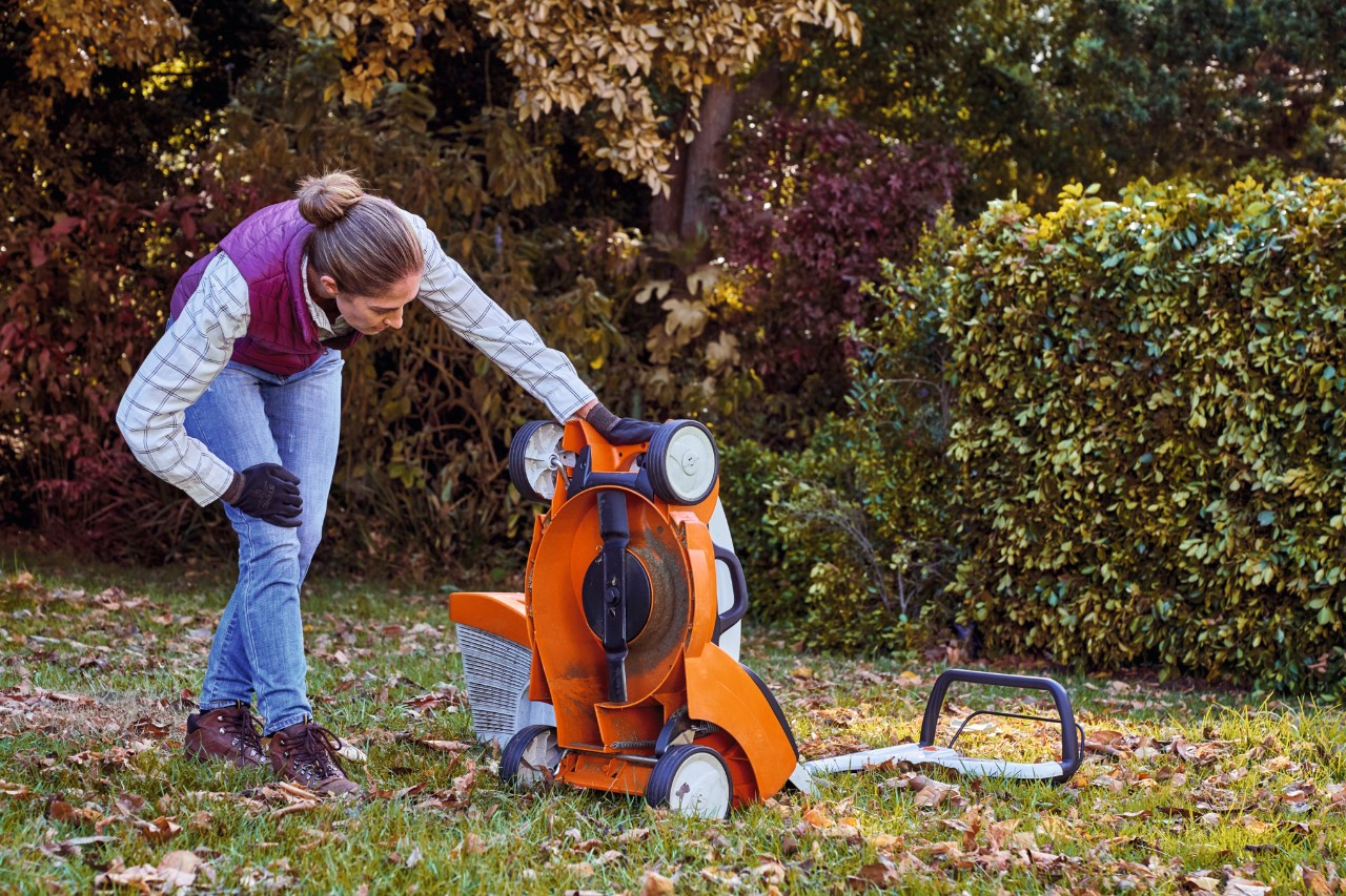 Žena na zahradě kontroluje spodní část akumulátorové sekačky STIHL RMA 339 C při podzimní péči o trávník 