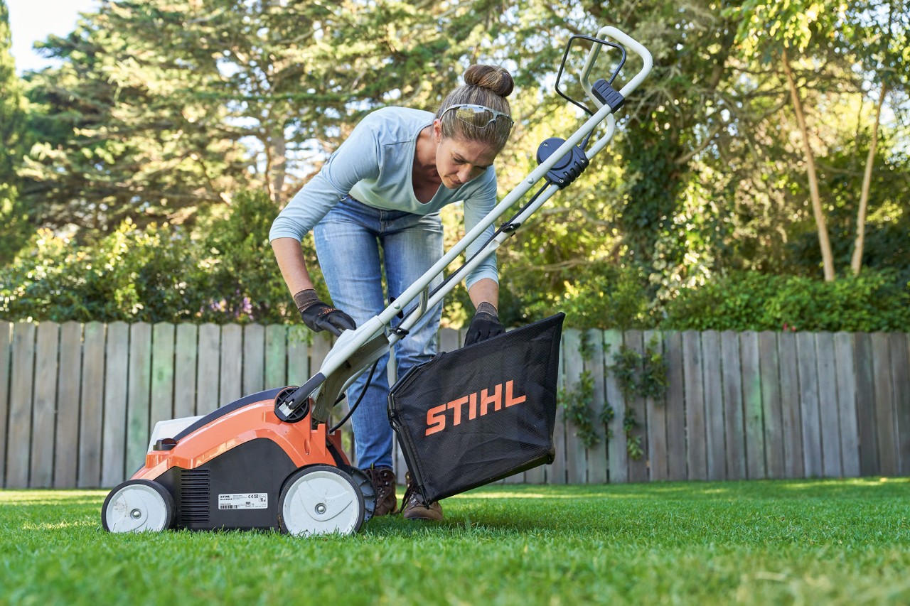 Žena připevňuje sběrný koš akumulátorového provzdušňovače trávníku STIHL RLA 240 k zadní části zařízení.