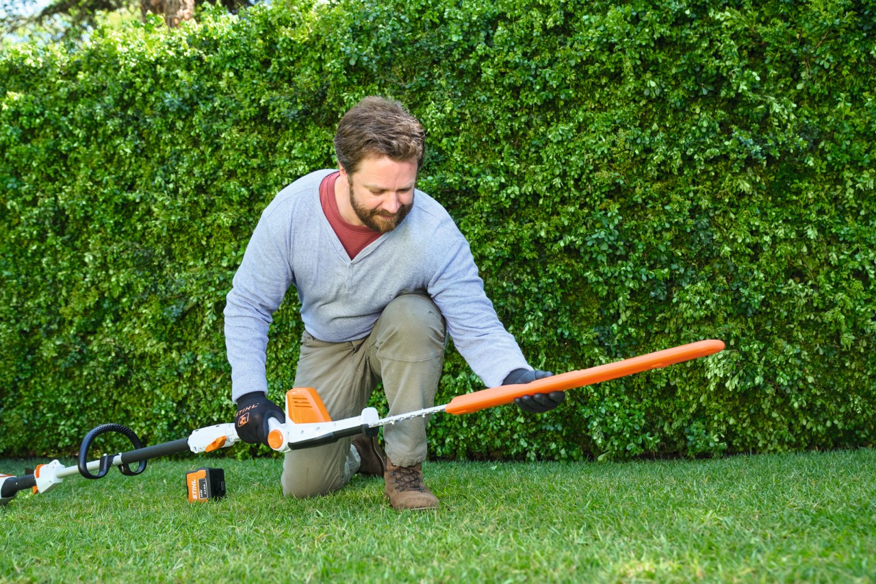 Muž před živým plotem pokládá na trávník akumulátorové nůžky na živý plot STIHL HLA 56
