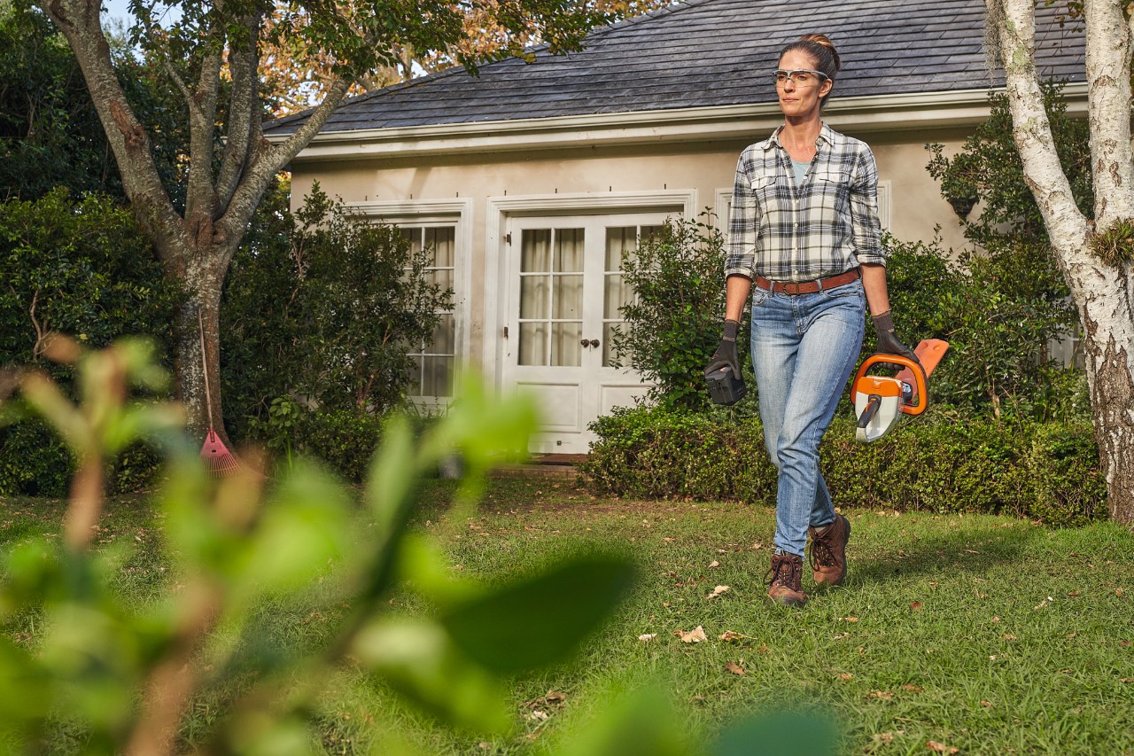 Žena kráčí po trávníku před domem s nůžkami na živý plot STIHL