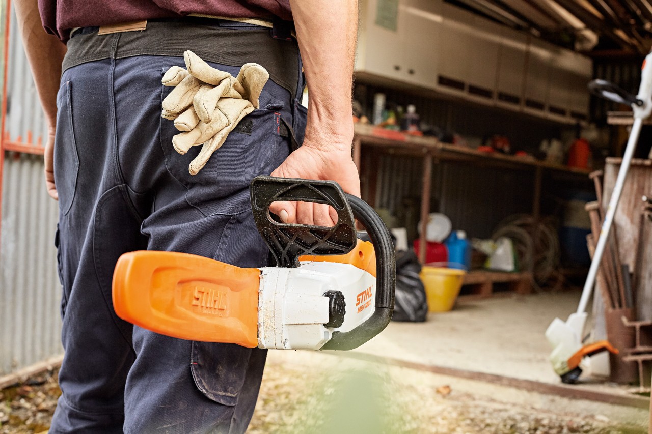 Muž stojí před dílnou s akumulátorovou řetězovou pilou STIHL s ochrannou lištou