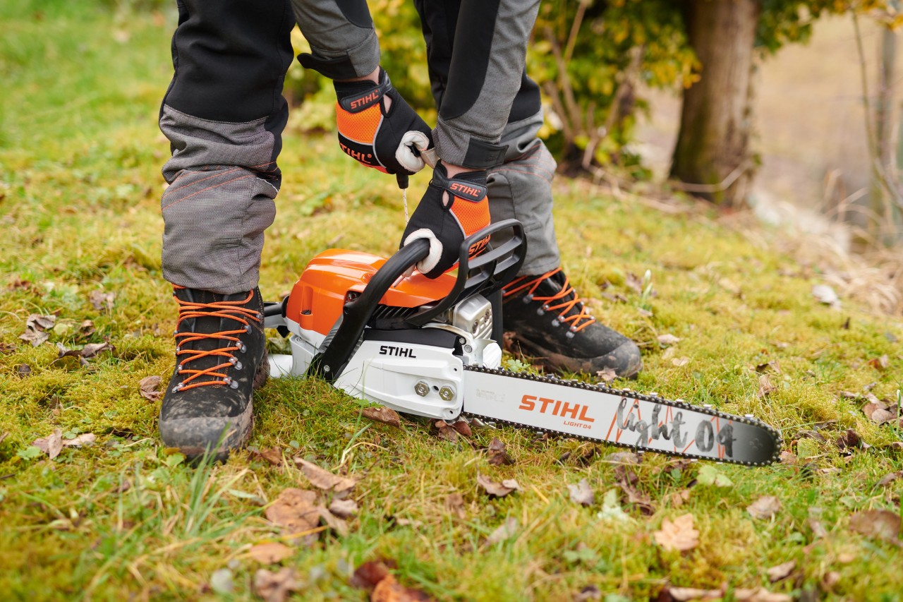 Řetězová pila STIHL MS261CM byla umístěna na zem v lese, aby ji pak mohla osoba bezpečně nastartovat.