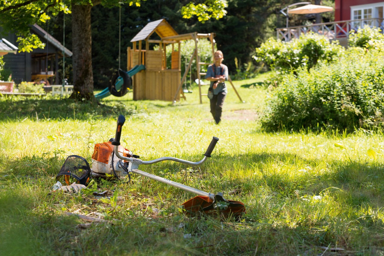 Křovinořez STIHL FS 240 leží v trávě, v pozadí se muž připravuje na údržbu