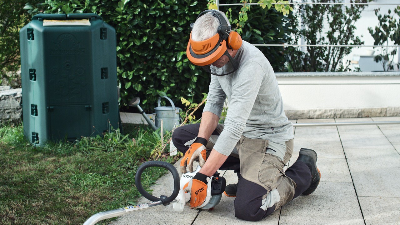 Benzinový vyžínač STIHL FS 38 přitlačuje k zemi osoba v ochranném oděvu