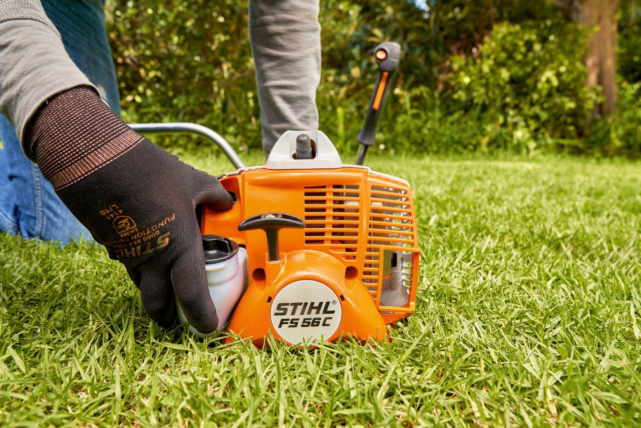 Muž tiskne palivové čerpadlo benzinového vyžínače STIHL FS 56, aby ho nastartoval
