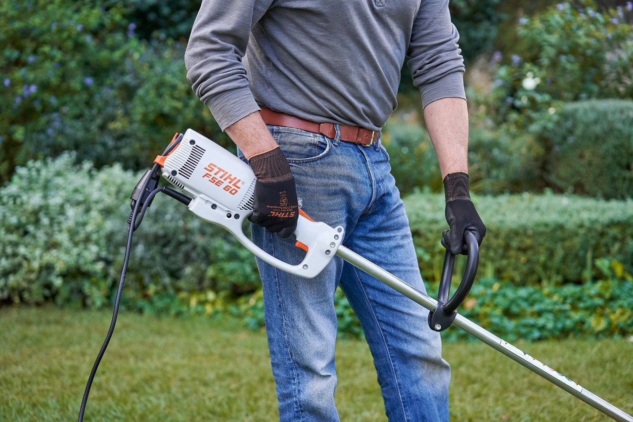 Muž v ochranných rukavicích drží elektrický vyžínač STIHL FSE 60 oběma rukama