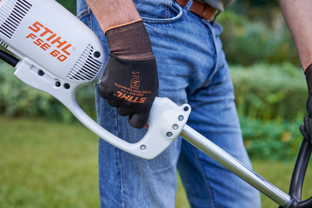 Muž tiskne spínač na ovládací rukojeti elektrického vyžínače STIHL FSE 60
