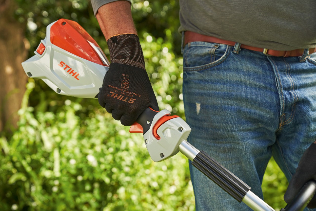 Muž v ochranných rukavicích mačká ergo-páčku akumulátorového vyžínače STIHL FSA 60 