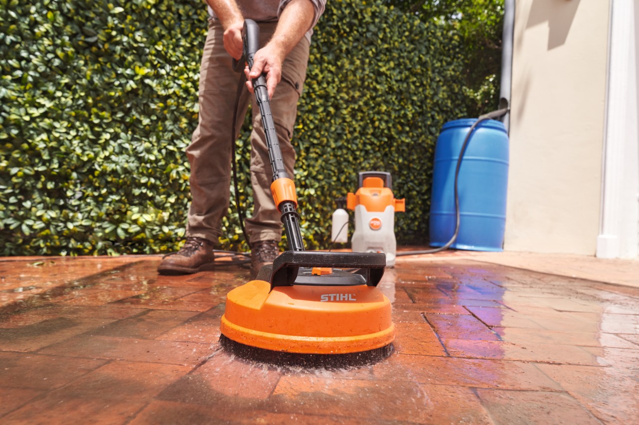 Detailní záběr elektrického vysokotlakého čističe STIHL RE 80 X, který čistí dlažební kostky na terase
