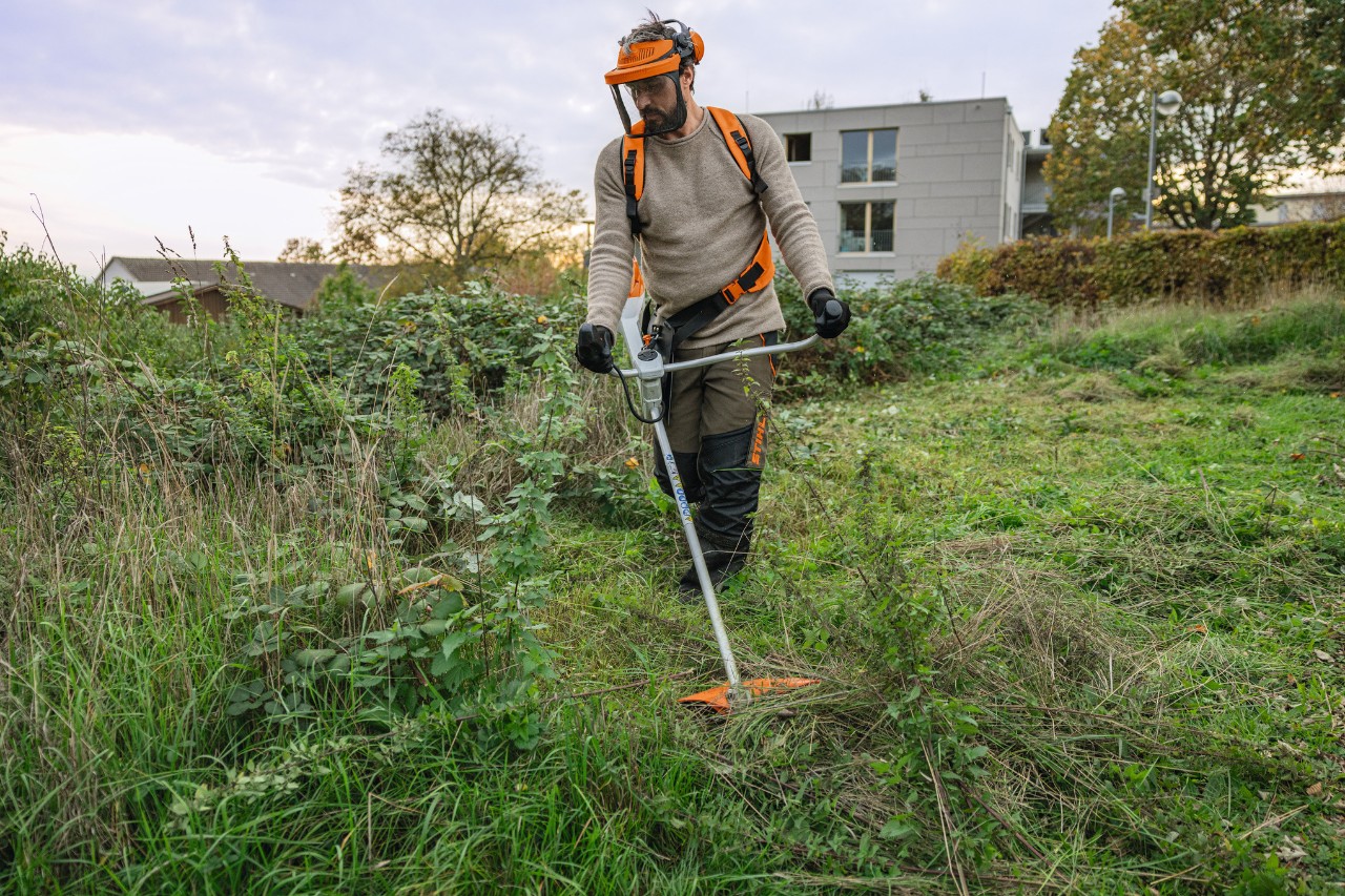 Muž s ochrannými pomůckami STIHL seče zelenou plochu s bujným porostem akumulátorovým křovinořezem STIHL FSA 200