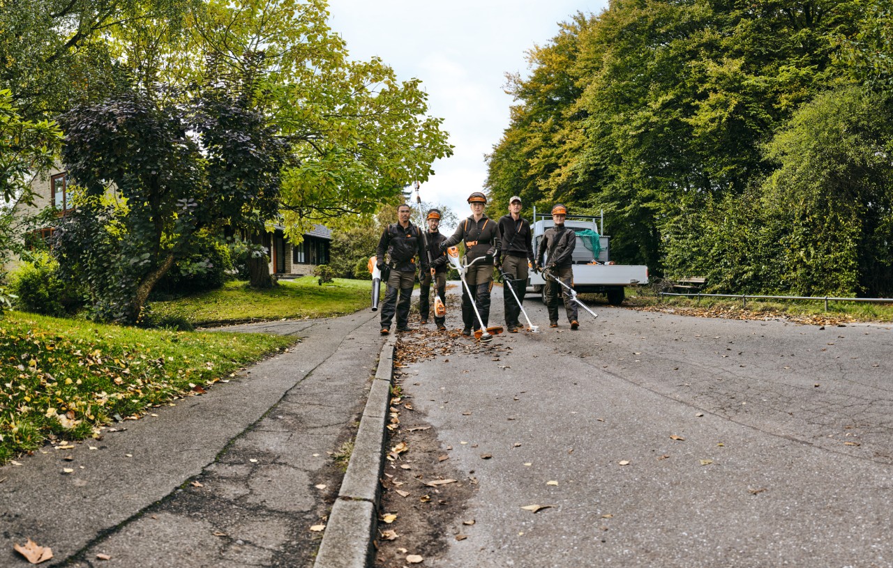 Pět osob v ochranných pomůckách STIHL kráčí vedle sebe po cestě s různým akumulátorovým nářadím STIHL.
