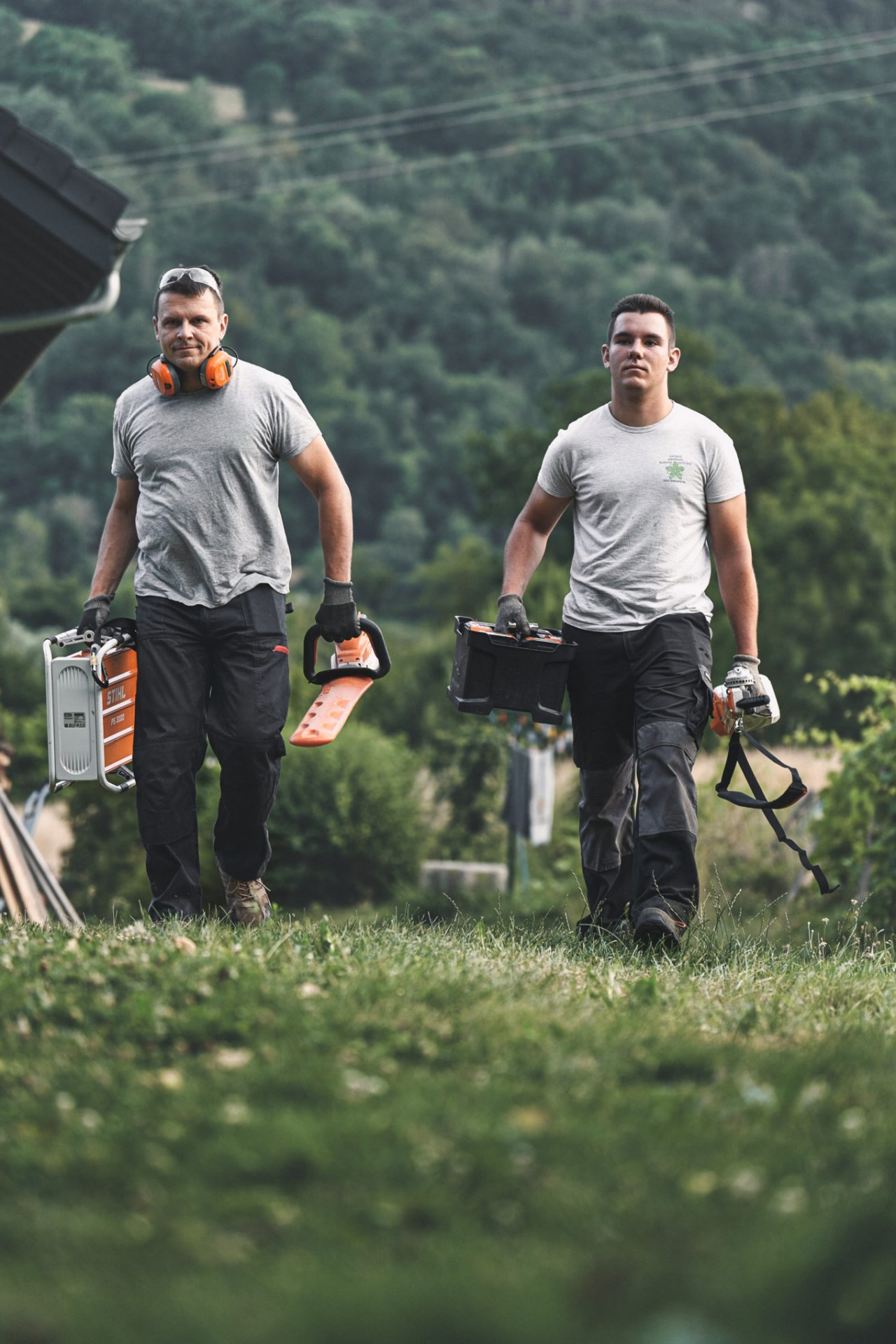 Dva profesionálové s akumulátorovým nářadím STIHL kráčejí po louce