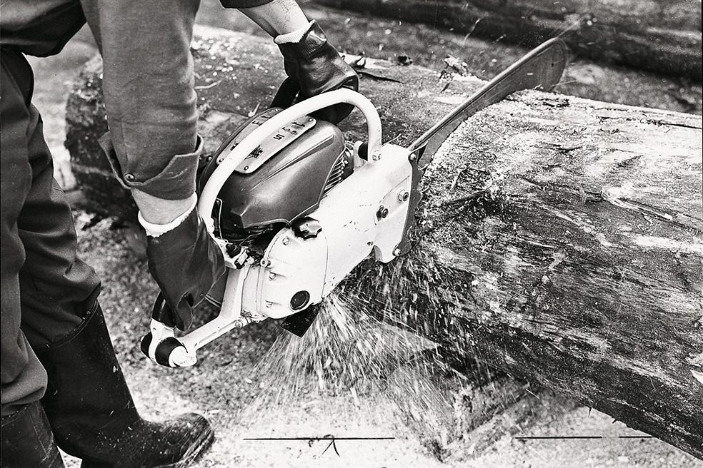 Stará černobílá fotografie muže, který řeže strom motorovou pilou STIHL Contra 