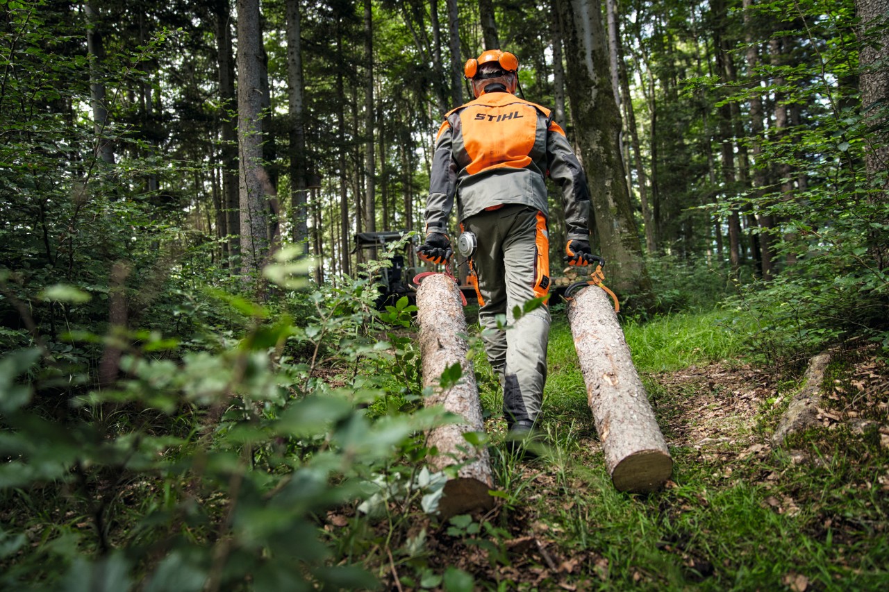 Lesník s ochranným vybavením STIHL při přepravě dřeva po lesní cestě