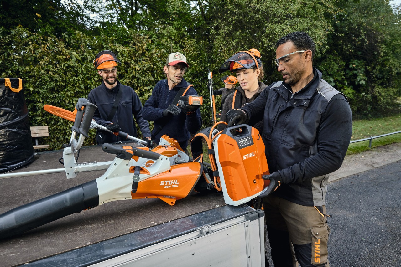 Tři muži a jedna žena v ochranných oděvech STIHL stojí na ložné ploše vozidla s vybavením STIHL, například akumulátorovým foukačem STIHL BGA 200 a zádovým akumulátorem STIHL AR 2000 L 