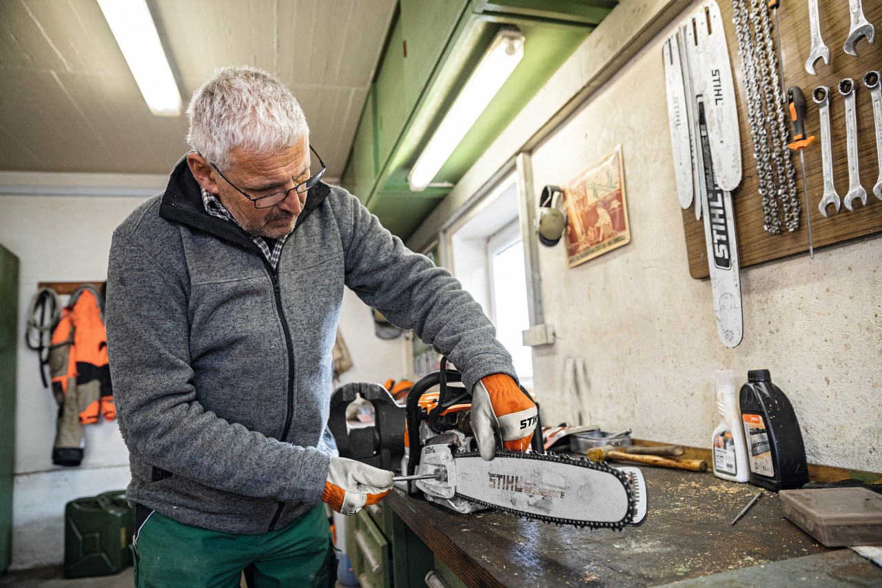 Muž v dílně provádí šroubování na motorové pile s vodicí lištou STIHL Rollomatic E. 