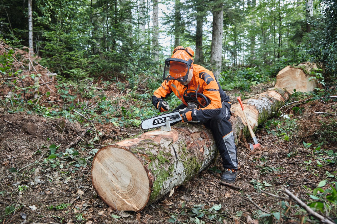 Muž v ochranných pomůckách používá motorovou pilu STIHL s plnou lištou k řezání již pokáceného stromu.