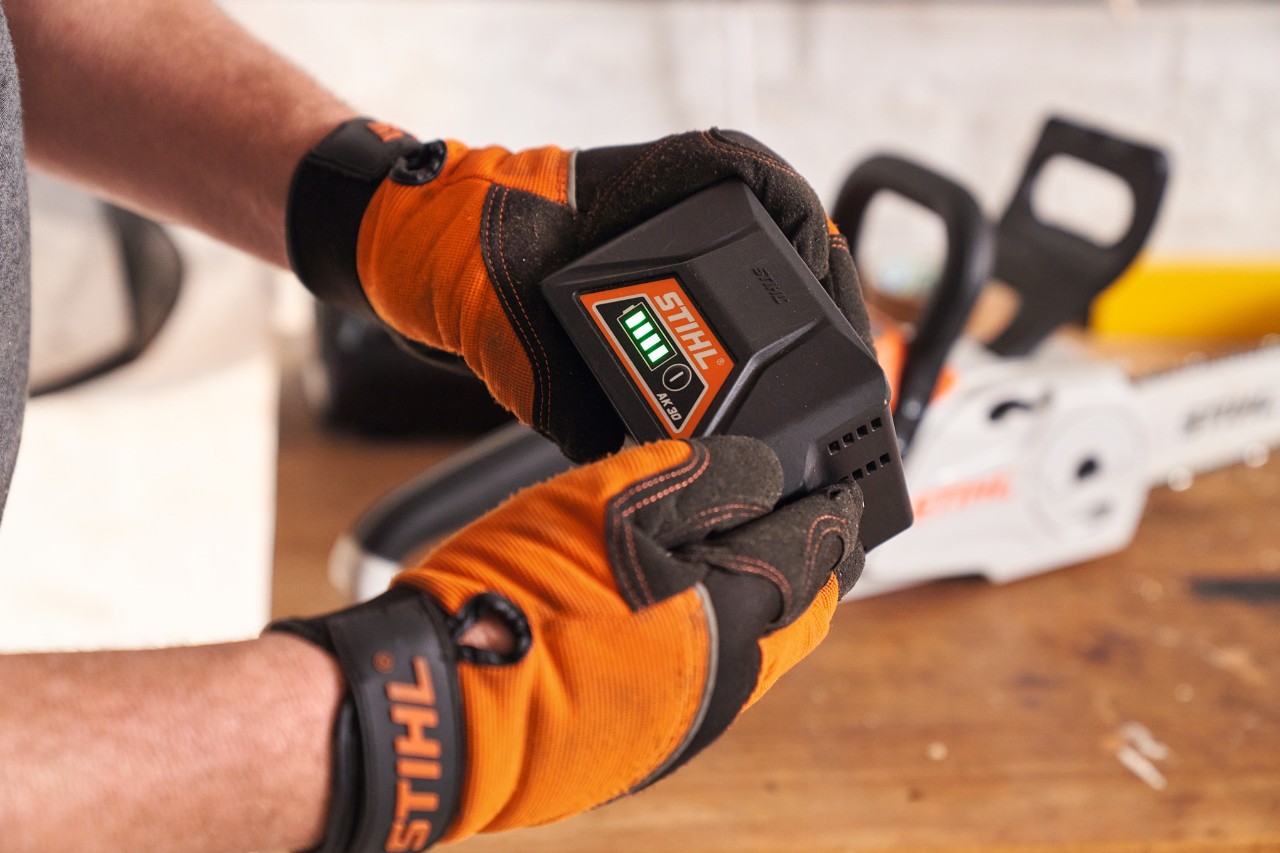 Osoba v ochranných rukavicích STIHL drží v rukou lithium-iontový akumulátor STIHL