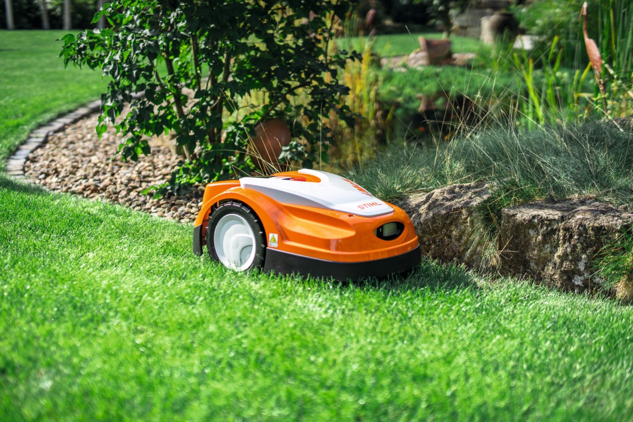 Sekačka STIHL iMOW RMI 422 seče trávník v zahradě na okraji malé kamenné zídky.