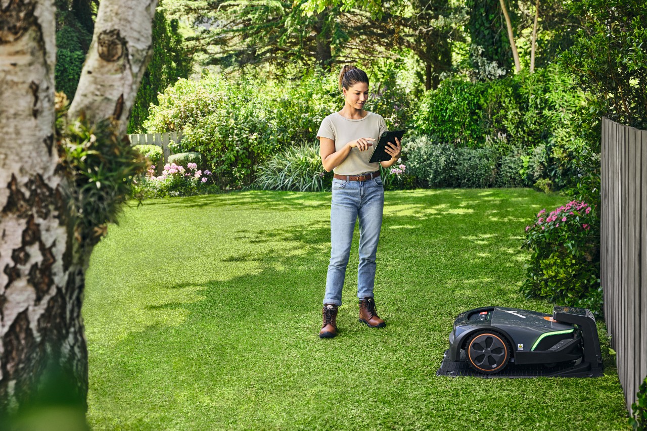 Žena obsluhuje na zahradě sekačku STIHL iMOW® EVO pomocí tabletu