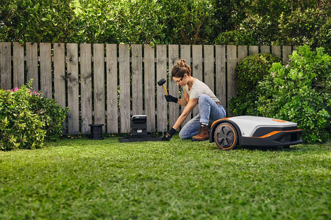 Žena si na své zahradě sama instaluje dokovací stanici pro sekačku STIHL iMOW® před plotem.
