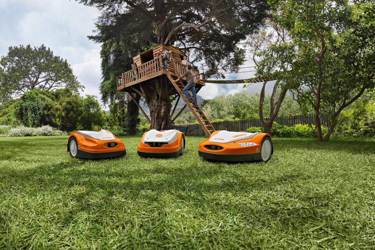 Různé robotické sekačky STIHL iMOW® na zeleném trávníku v zahradě