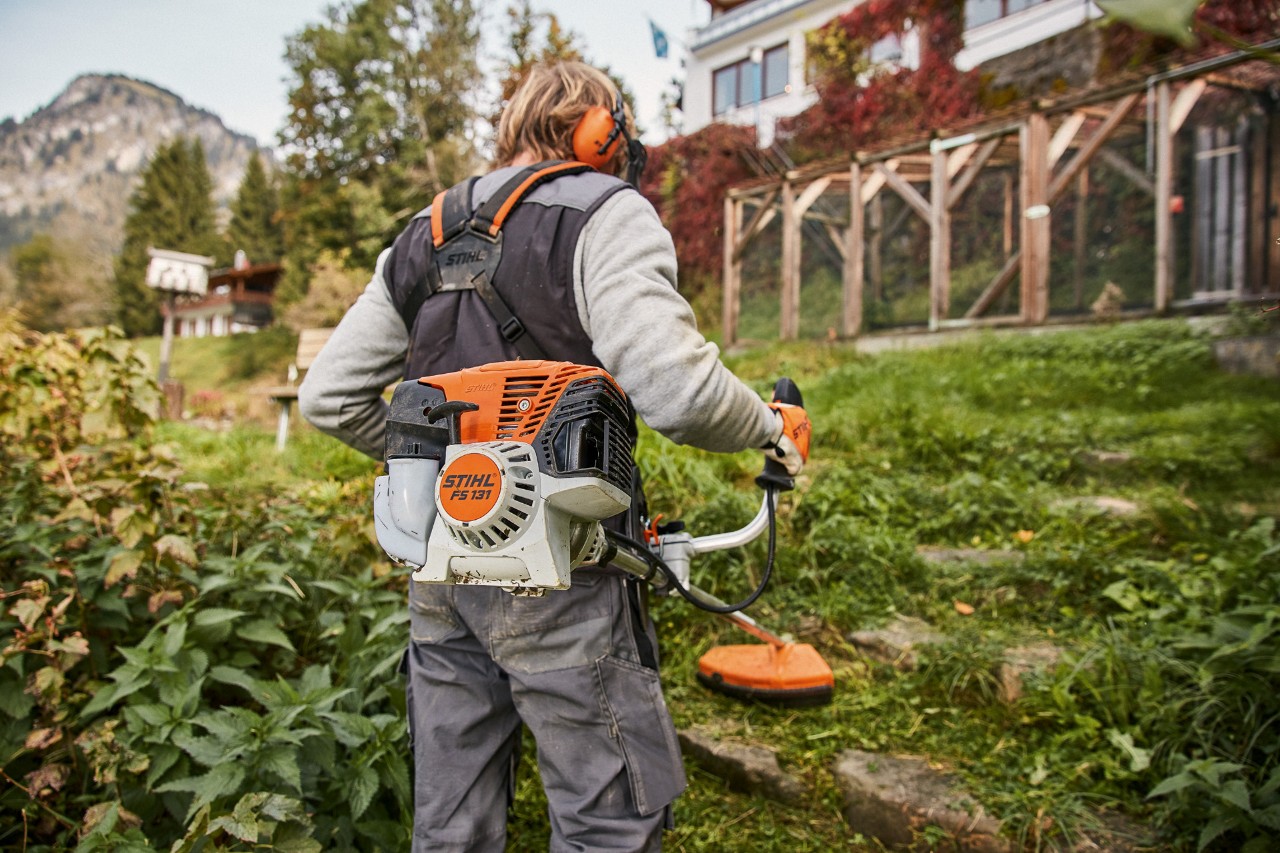 Svažitý terén před domem je sečen benzínovým křovinořezem STIHL FS 131 s motorem 4-Mix®